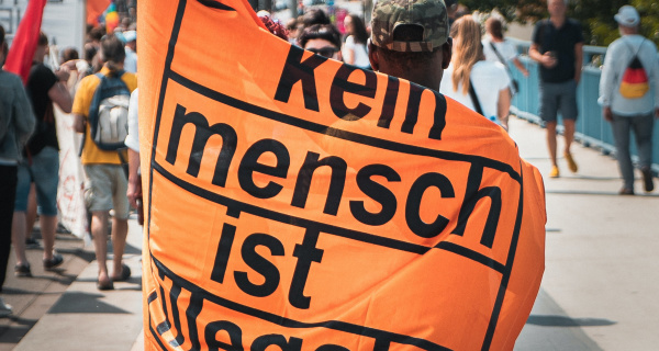 Demonstranten mit Plakat "Kein Mensch ist illegal". Foto: Mika Baumeister, unsplash.com, 9fJidQI2o-s